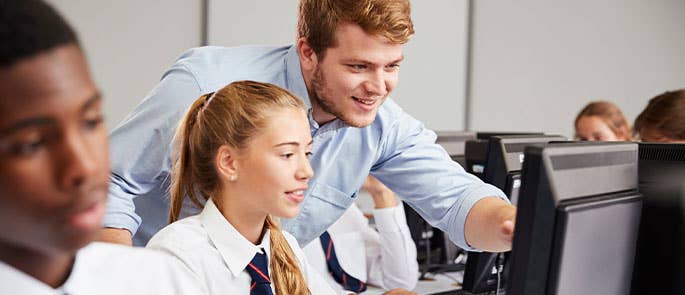 teacher helping a student with work on a computer in classroom