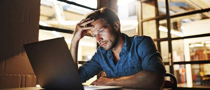 A man looking distressed working on his laptop
