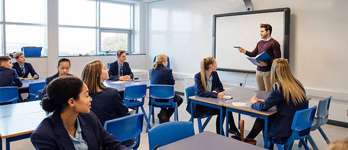 Secondary school teacher teaching at the front of classroom with smartboard