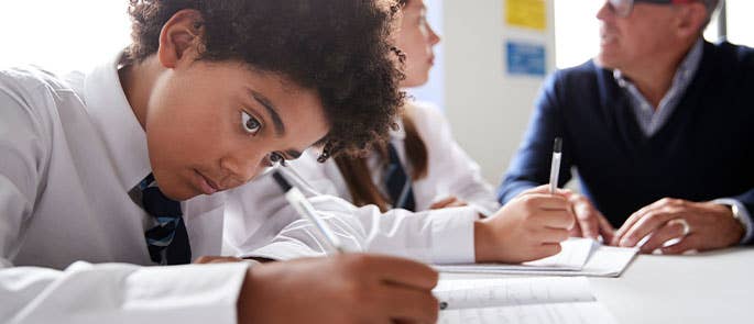 School child working in a classroom with teacher helping a student in the background with work