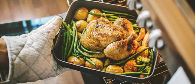 chef putting chicken and vegetables in oven to bake