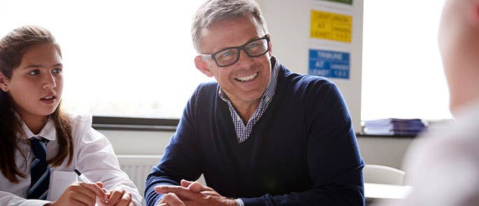 teacher sat at a table in classroom with students