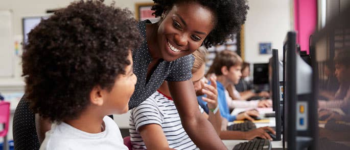 teacher instructing and aiding a child at a computer in the classroom