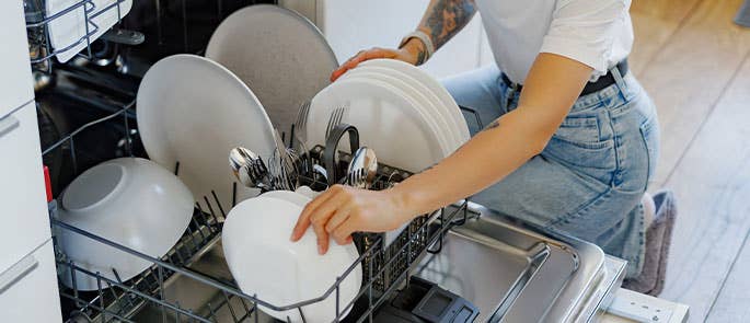 Person loading plates onto the bottom rack of a dishwasher