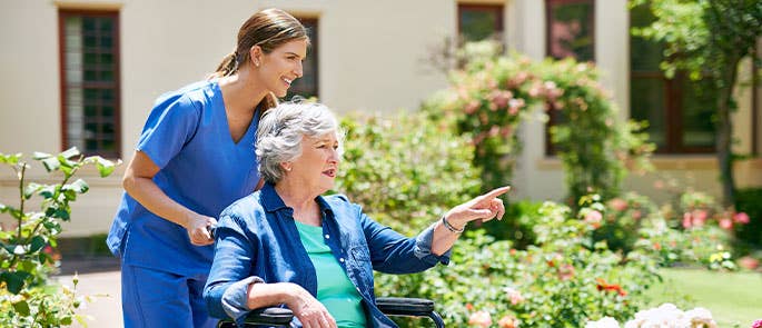 Health and social care worker pushing elderly person in wheelchair outside care home