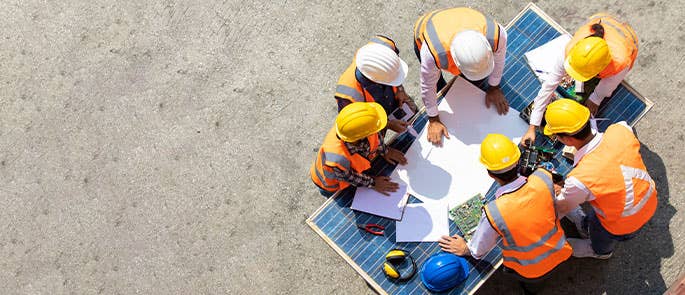 Group of labourers and construction workers on a site gathered around construction plans in PPE