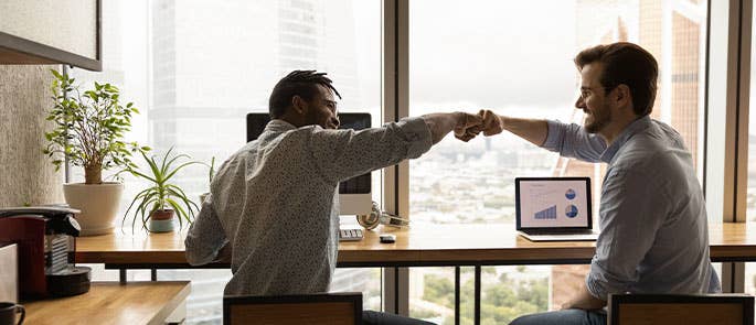 two coworkers sat on laptops, fist bumping 