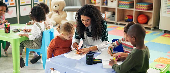 Teacher with children in classroom helping to colour in 