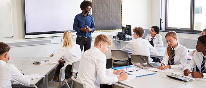 secondary school students in classroom working with teacher in front of whiteboard