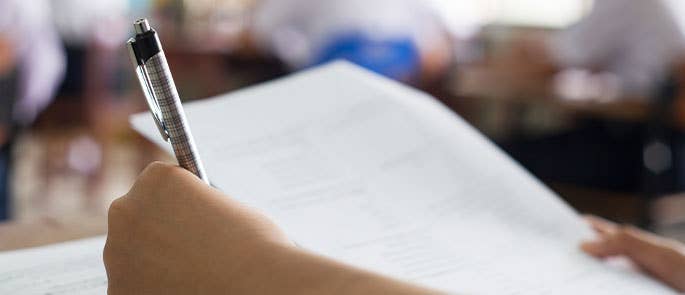 person writing with pen and paper in classroom