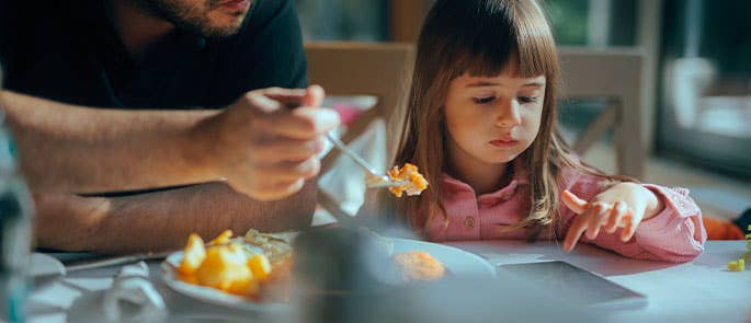 child scrolling on phone at the dinner table instead of eating food