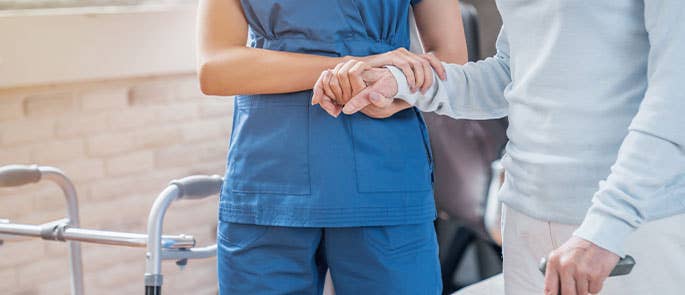 health and social care professional helping elderly patient to walk by holding their hand